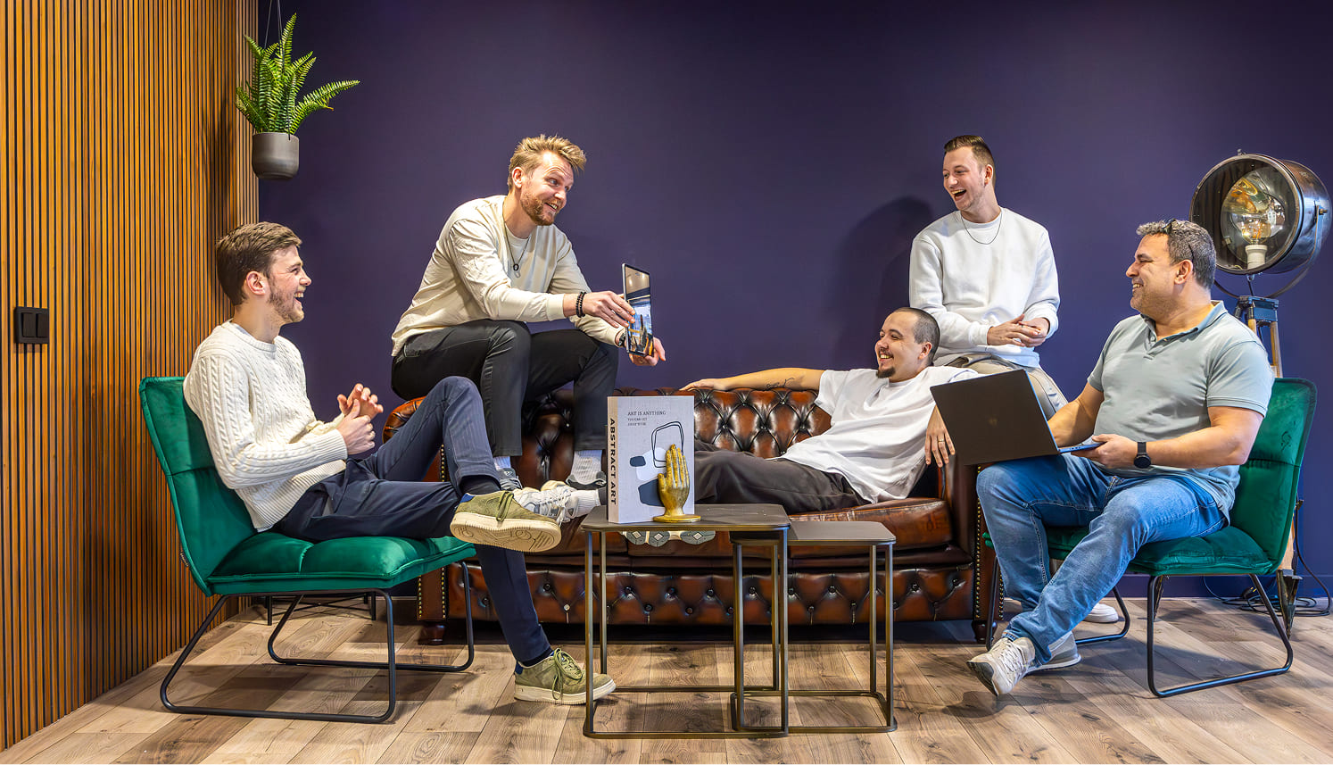 Het team van Scrolla! met vijf mensen die relaxen en elkaar dingen laten zien op een laptop en tablet